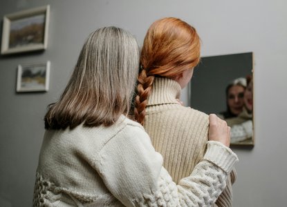 older-woman-holds-younger-womans-shoulders-looking-in-mirror.jpg