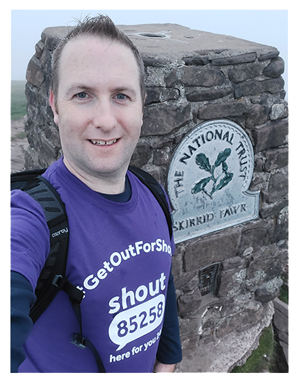 Fundraiser Andrew wears his purple Get Out For Shout t-shirt in a selfie at the peak of Skirrid Fawr