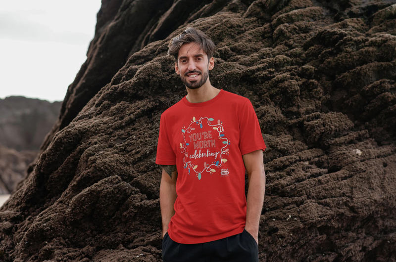 White man standing in front of rocks wearing a red t-shirt that says You&#x27;re Worth Celebrating